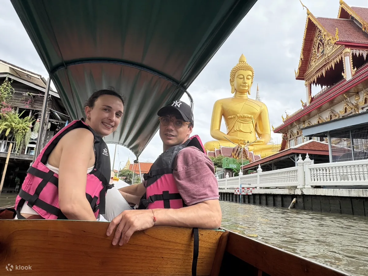 Two travelers in life jackets on the canal boat with the Big Buddha at Wat Paknam behind them
