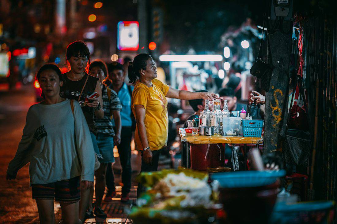 People walking past street food stalls in Bangkok at night