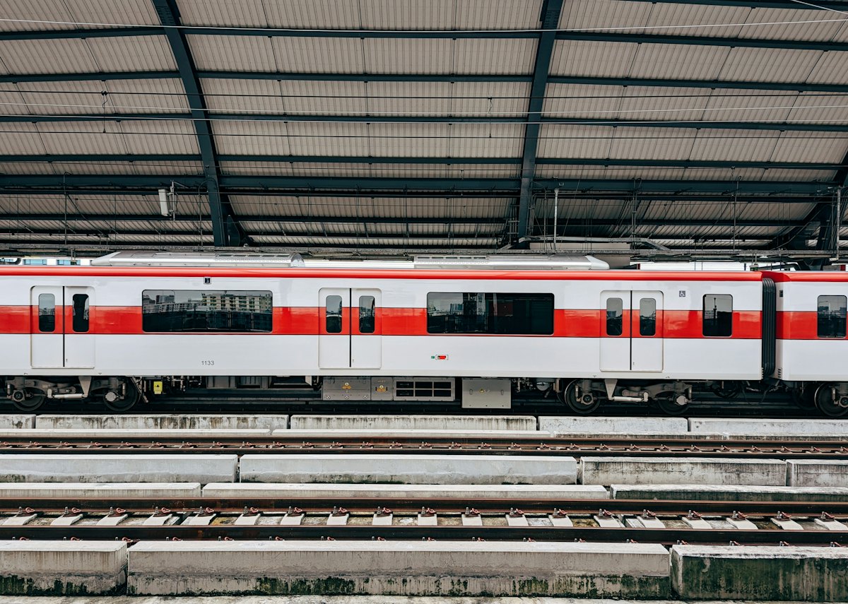 A red and white SRT Red Line train at a platform under the steel roof of a Bangkok station