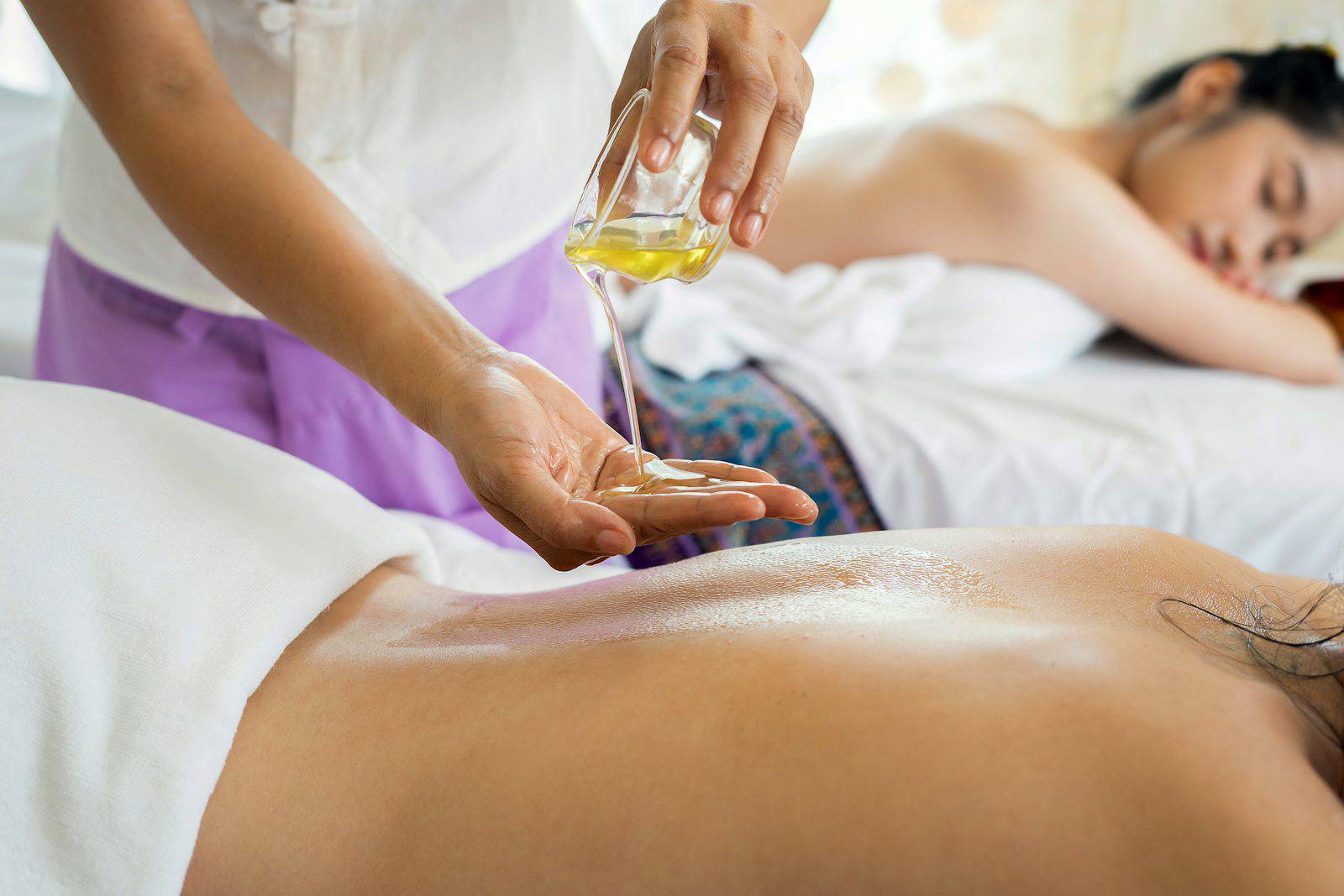 A candlelit spa treatment room with white towels and tropical flowers on a bamboo tray