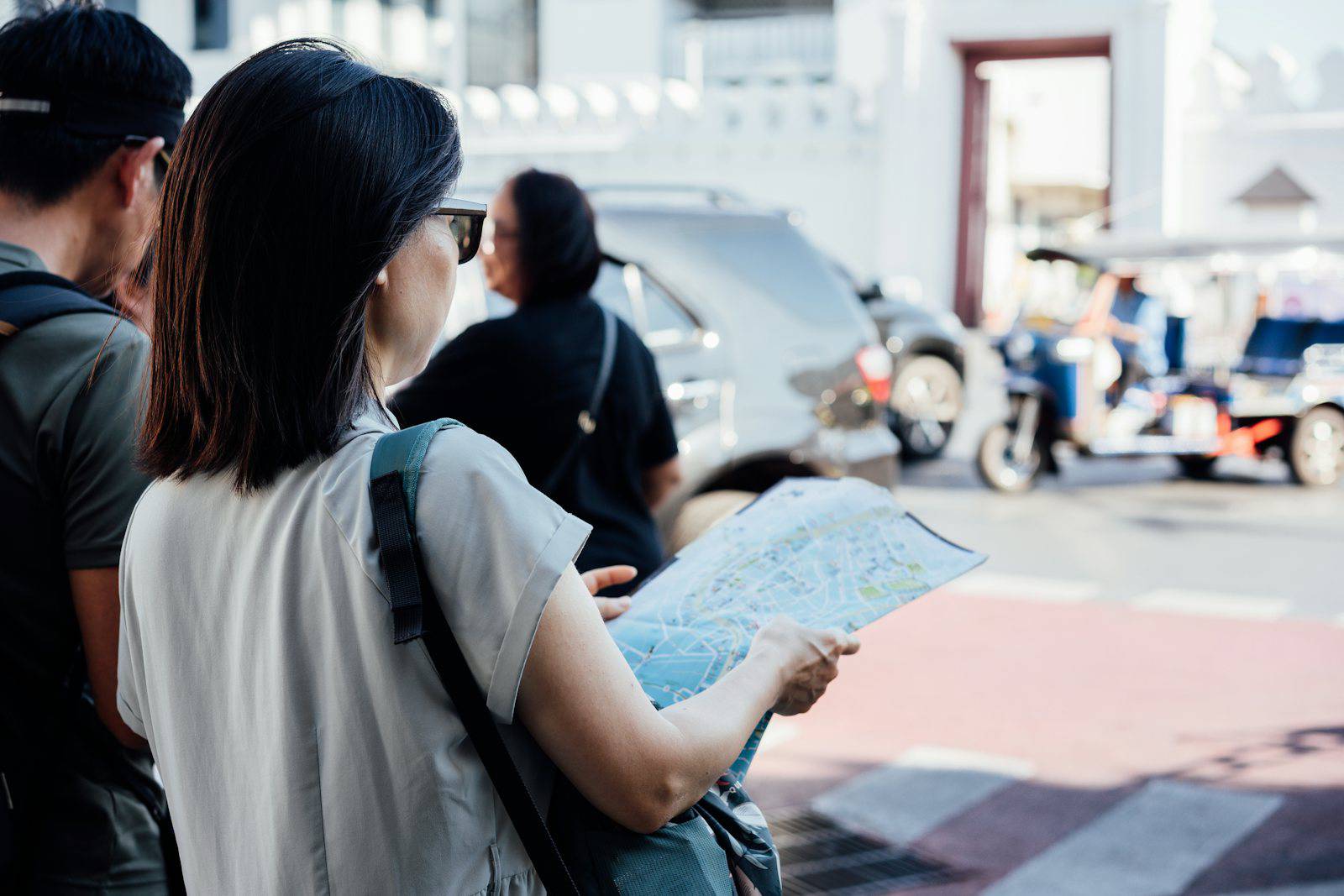 Travelers reading a map on a Bangkok street with a tuk tuk nearby