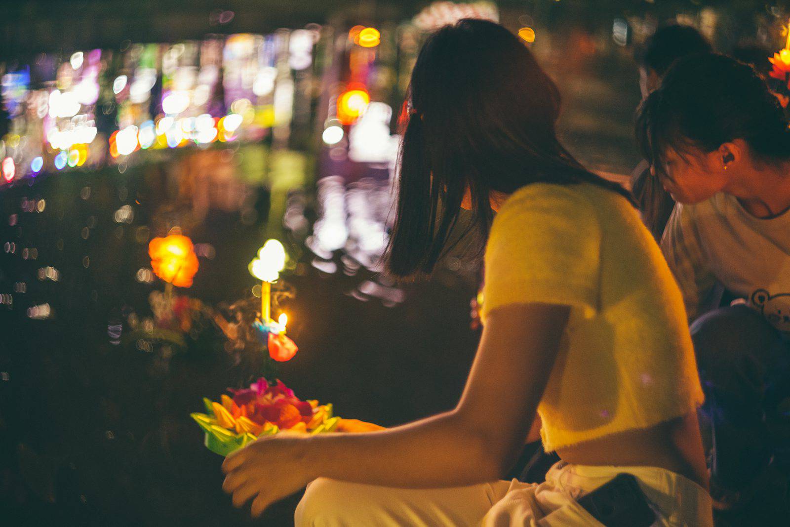 Woman holding a candlelit krathong by the water during Loy Krathong