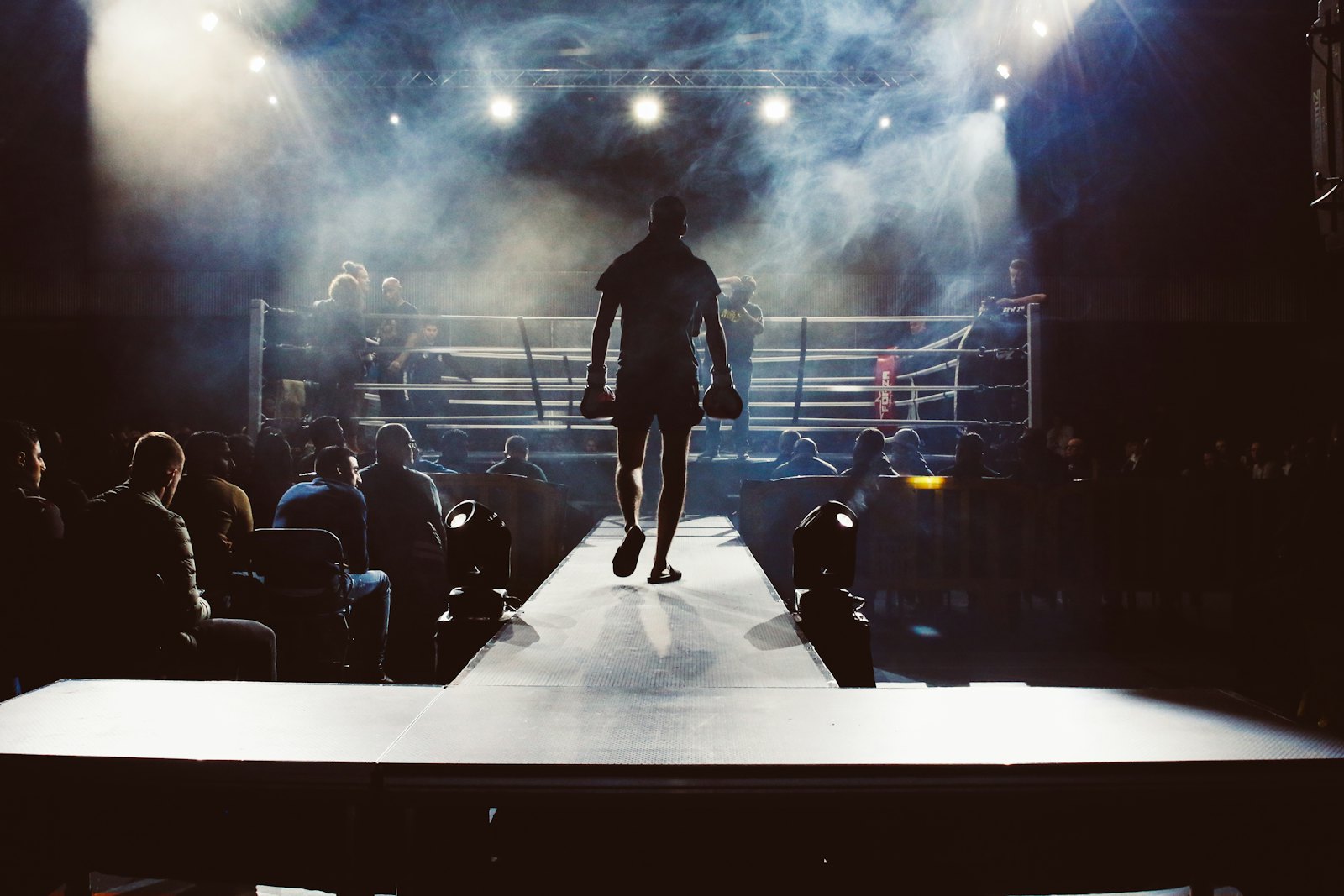 A fighter walking out to a floodlit boxing ring