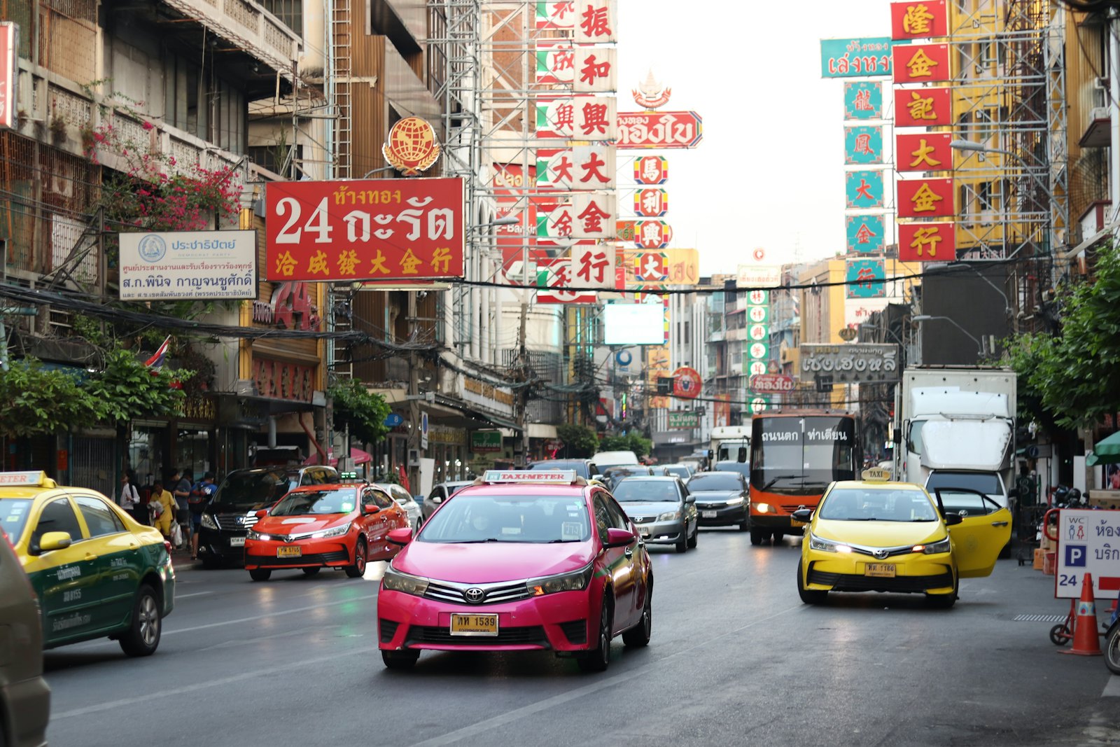 Pink and yellow-green Bangkok taxis in traffic on Yaowarat Road in Chinatown, under shop signs