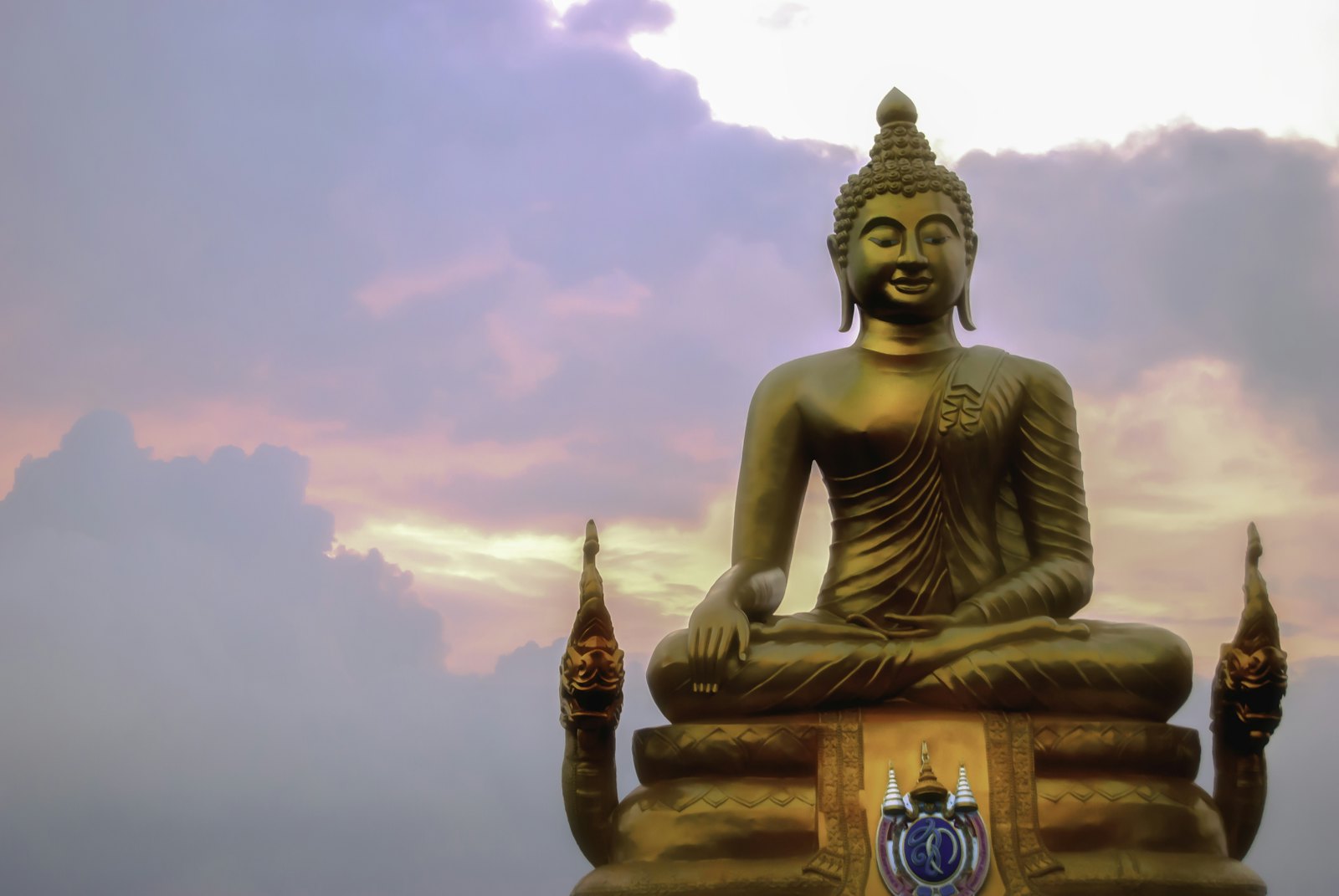 A large seated golden Buddha against a coloured sky