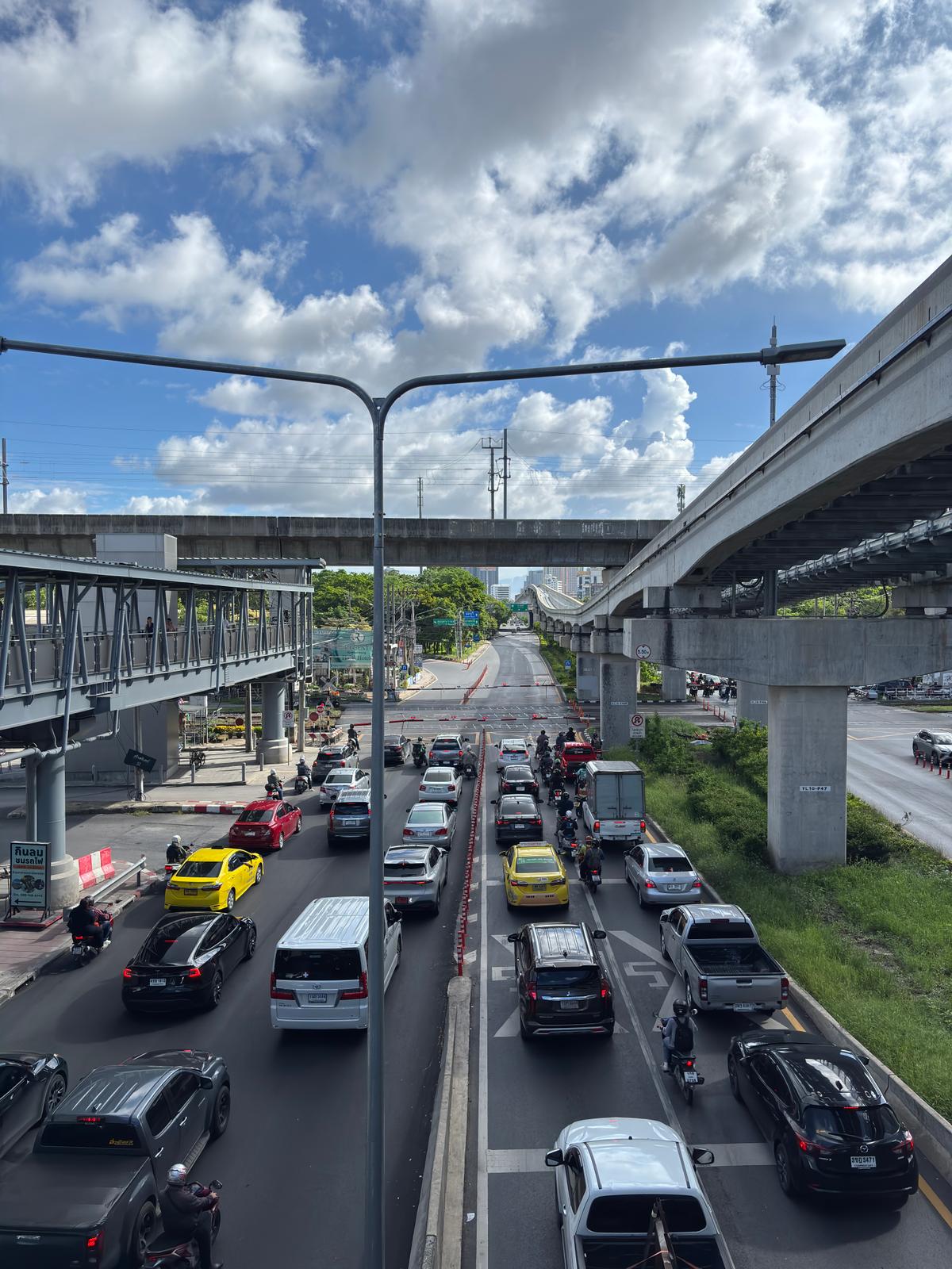 Yellow taxis and morning traffic queued under Bangkok's elevated rail lines and a footbridge