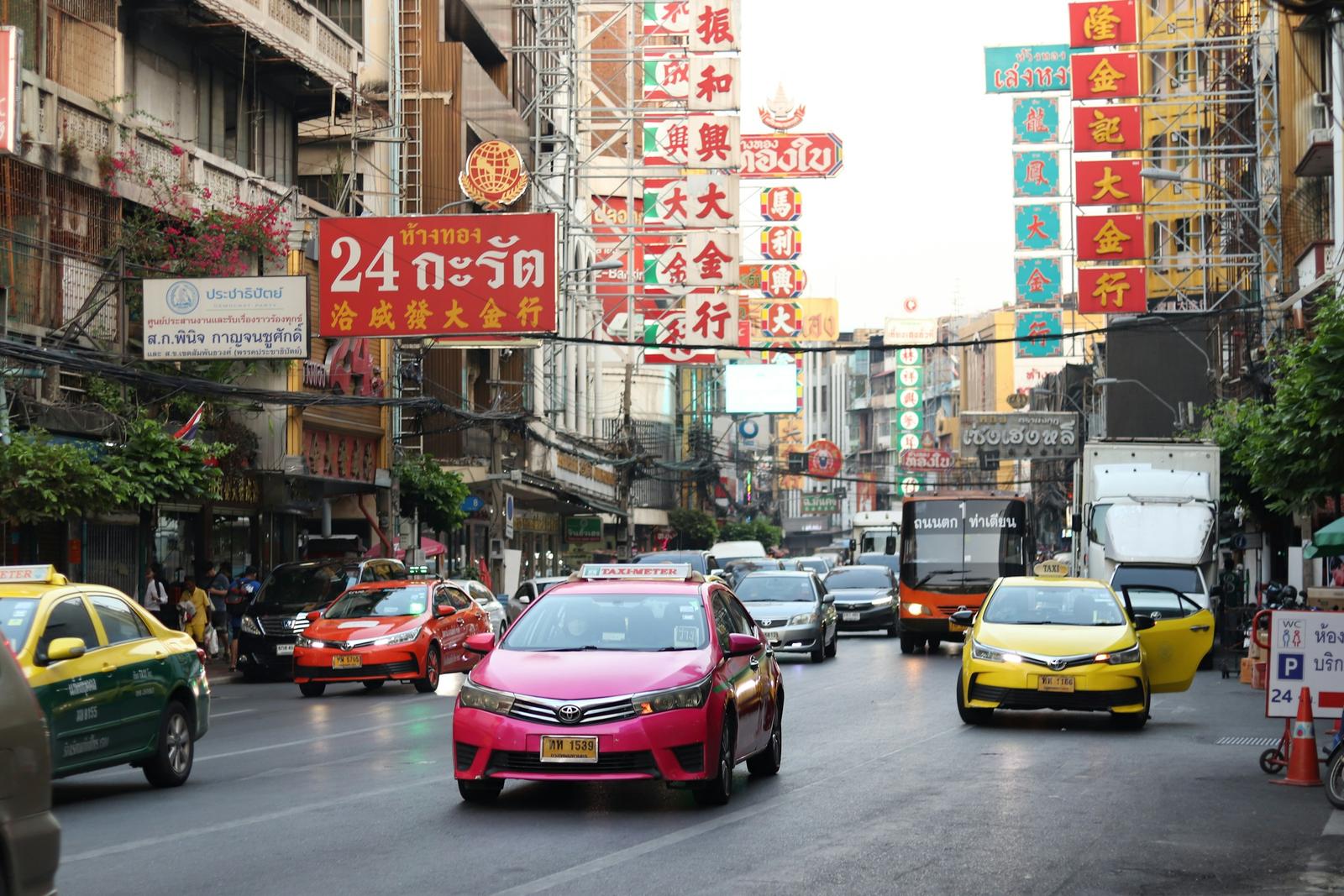 Pink and yellow taxis in daytime traffic on Yaowarat Road in Bangkok's Chinatown